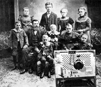 Black and white image of men Women and children in old, possibly 19th century, clothes watching a TV