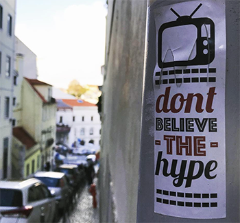 Sticker on lampost on Lisbon street: an image of TV with the words, Don't Believe the Hype